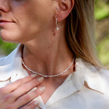Close-up of a person wearing a delicate necklace and earrings outdoors.
