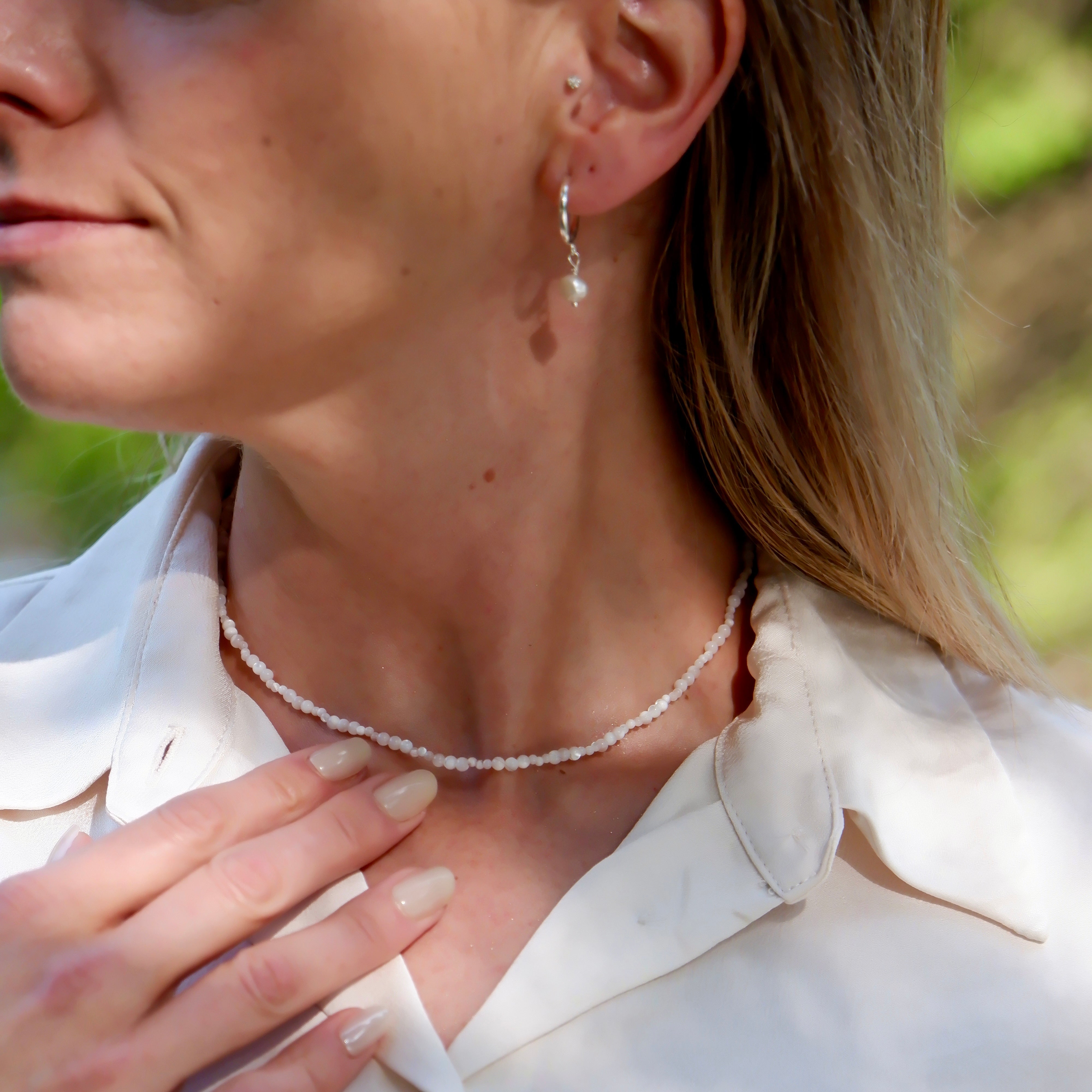 Close-up of a person wearing a delicate necklace and earrings outdoors.