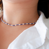 A close-up image of a person wearing a Midnight Tide choker necklace with deep blue sodalite beads and tiny freshwater rice pearls.