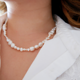 A close-up image of a person wearing a white pearl necklace with a soft focus on the pearls and an out-of-focus background.