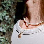 Close-up of a person wearing a gold necklace and pearl bracelet with a blurred natural background
