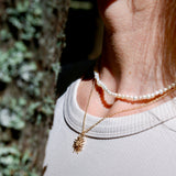 Close-up of a person wearing a gold necklace and pearl bracelet with a blurred natural background