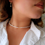 A person wearing a white chocker necklace with rice-shaped mother of pearl beads and gold-plated crimp end beads.