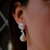 A close-up of a person's ear wearing a double-drop pearl earring with a small silver accent, paired with a matching pearl necklace.