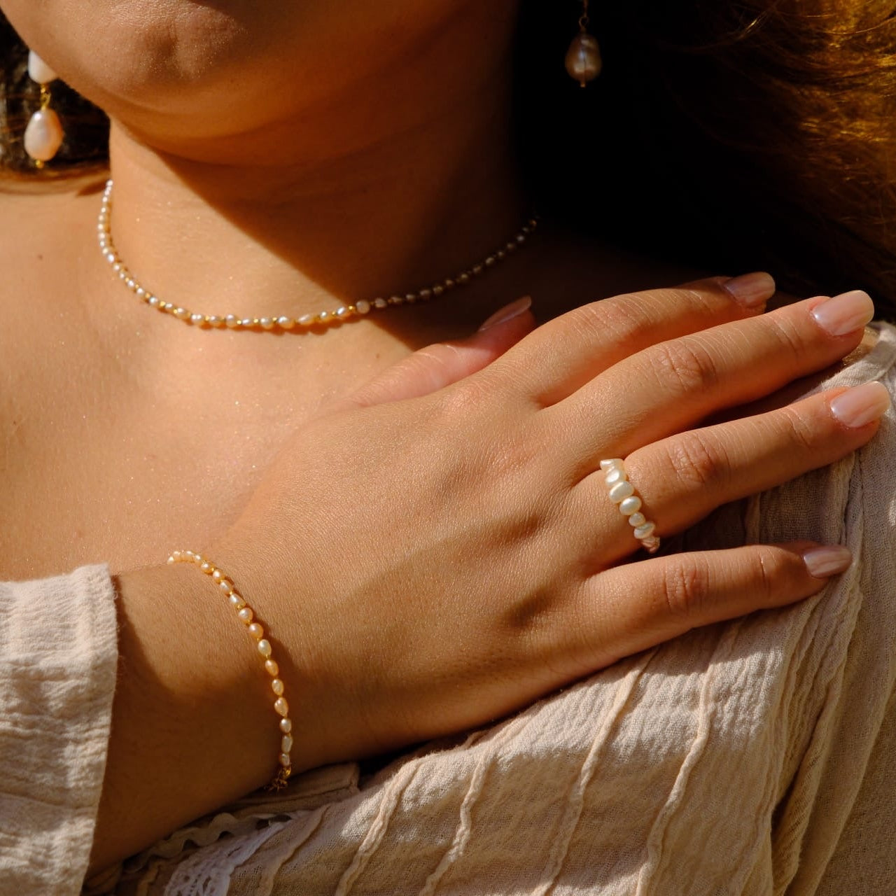 A close-up lifestyle shot of a woman wearing a matching jewelry set, featuring a delicate gold chain necklace, a gold beaded bracelet, and a gold beaded ring on her finger.