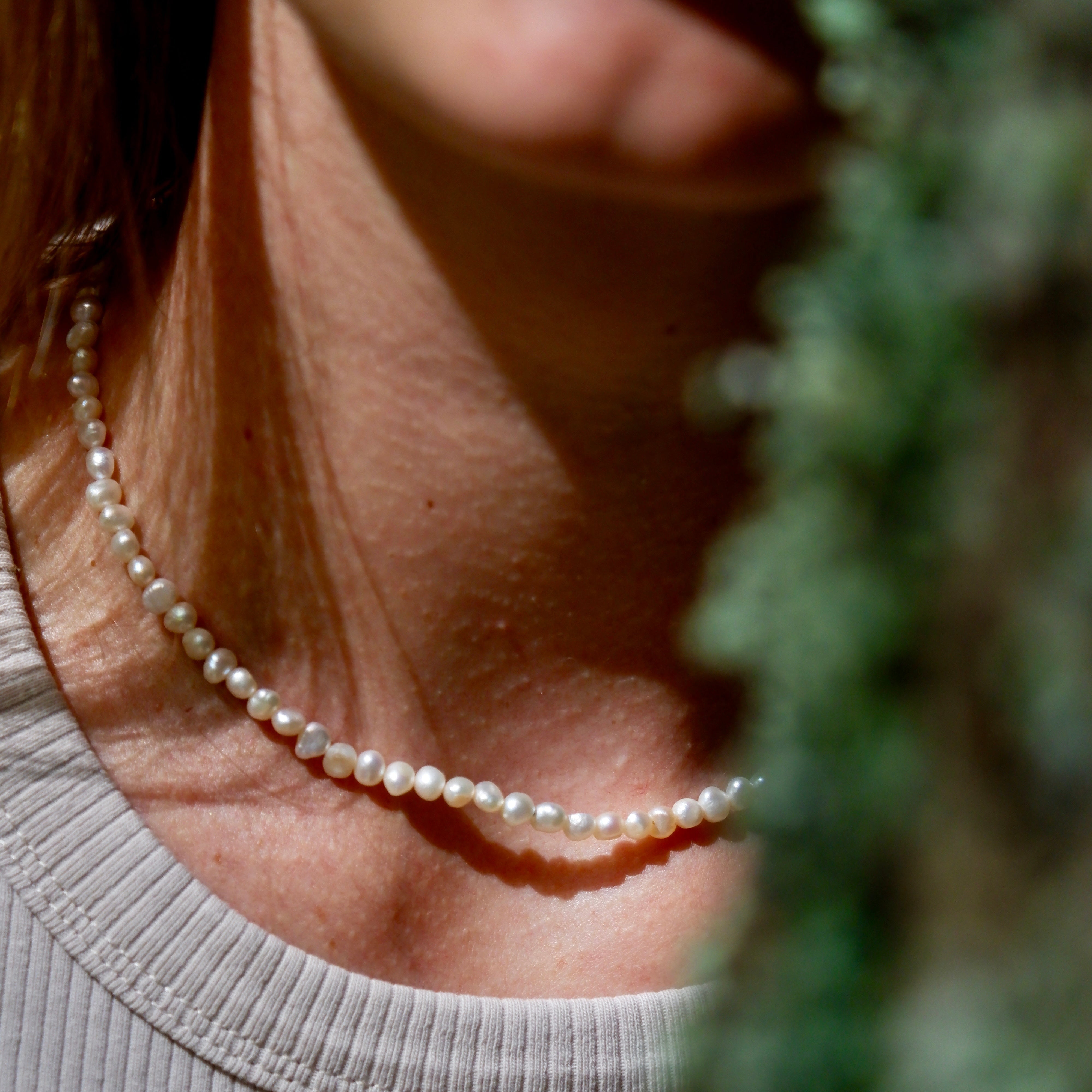 Pearl necklace worn by a person with a blurred green background