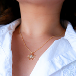 Gold necklace with a pendant worn by a person in a white shirt.