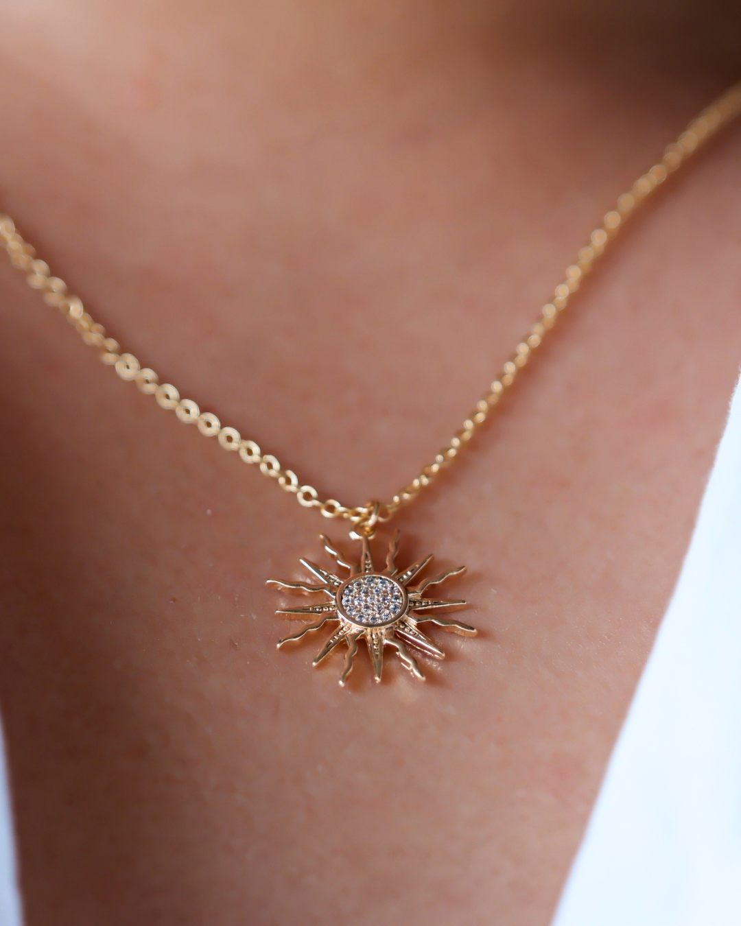 Gold necklace with a sun-shaped pendant on a person's neck.