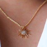 Gold necklace with a sun-shaped pendant on a person's neck.