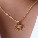 Gold necklace with a sun-shaped pendant on a person's neck.
