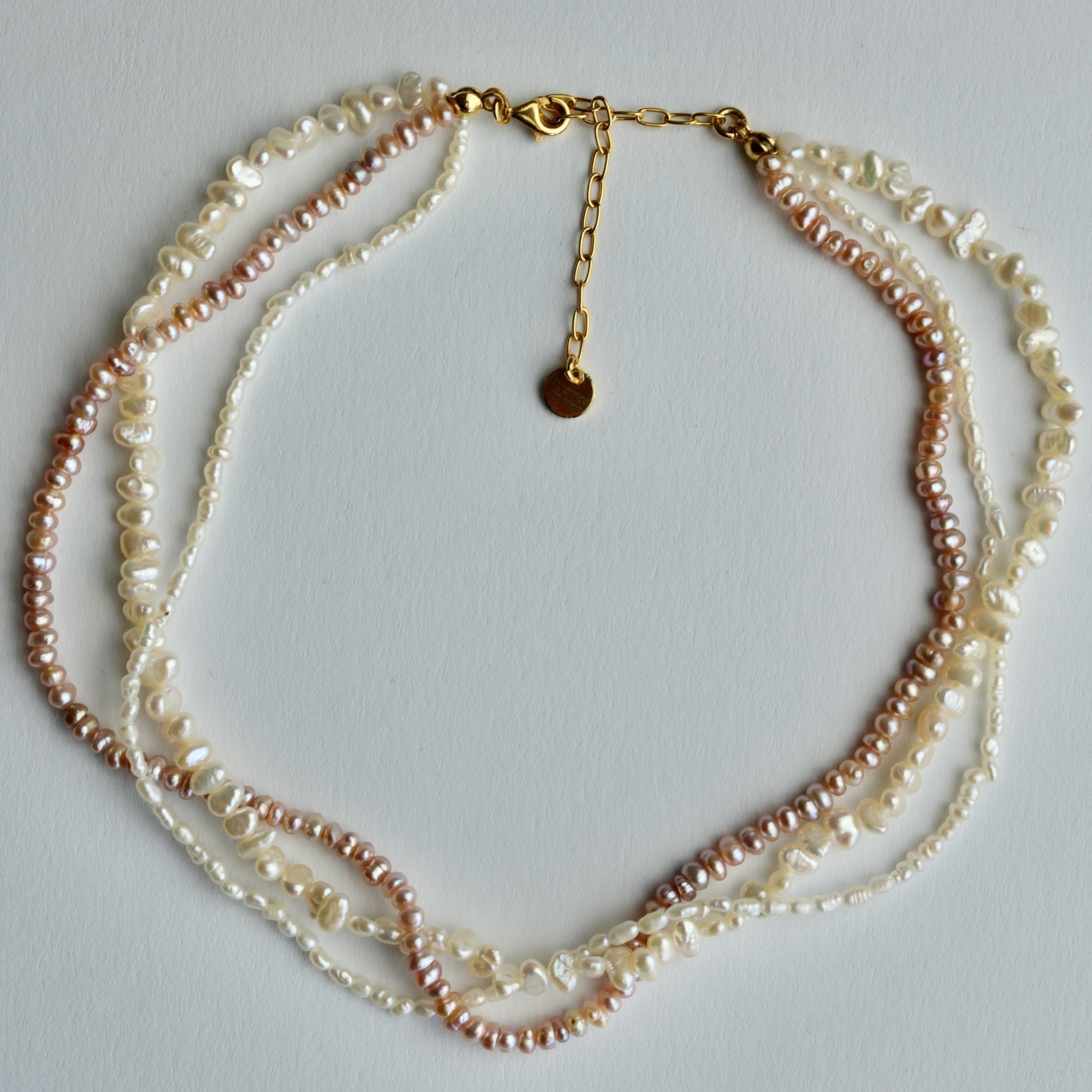A multi-strand pearl necklace featuring strands of cream, white, and light pink freshwater pearls with a gold-tone chain and clasp, displayed on a light gray background.