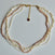 A multi-strand pearl necklace featuring strands of cream, white, and light pink freshwater pearls with a gold-tone chain and clasp, displayed on a light gray background.