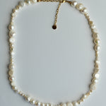 A mixed-size freshwater pearl necklace with a gold chain extender and a small round gold tag, displayed on a light gray background.