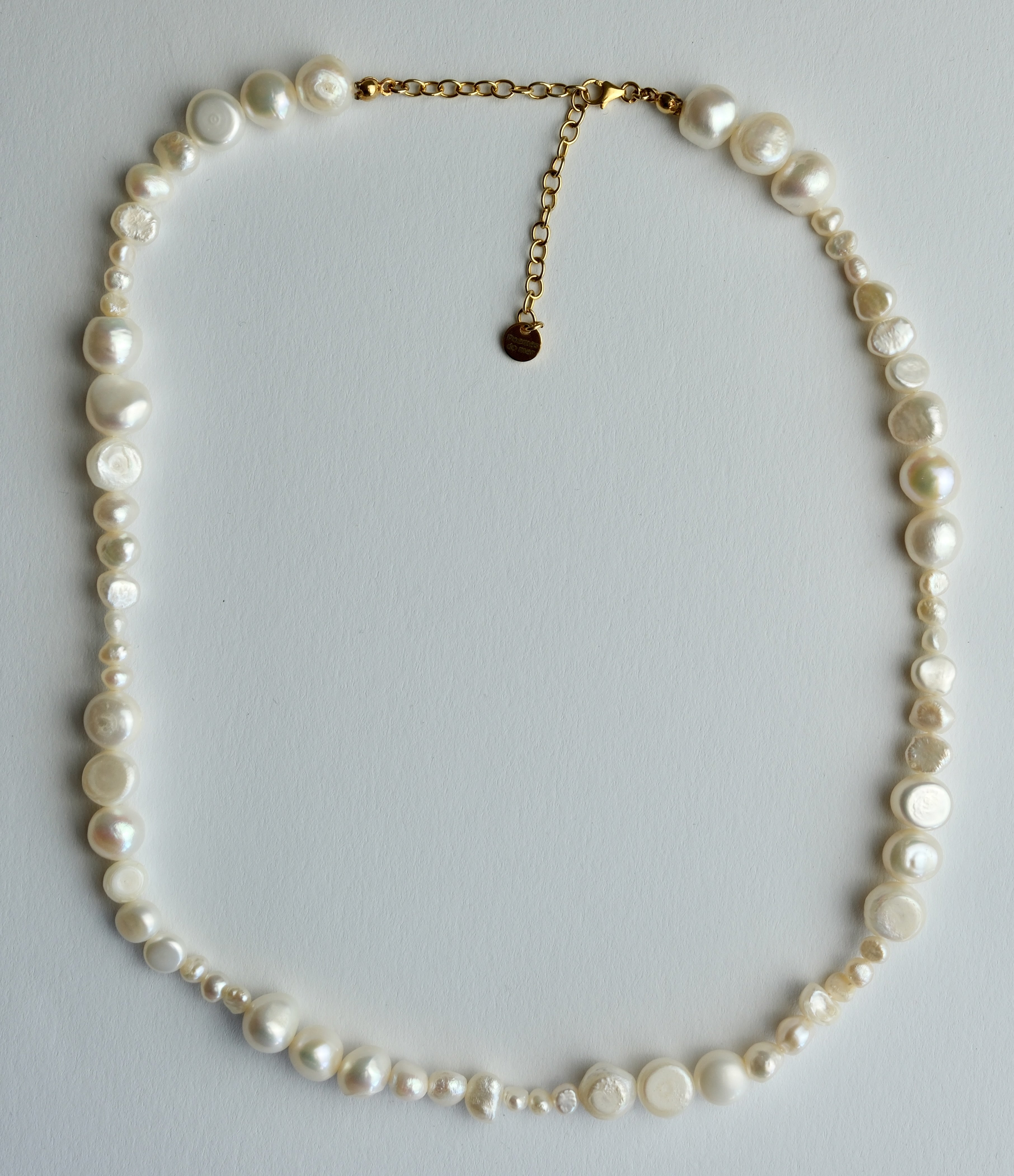 A mixed-size freshwater pearl necklace with a gold chain extender and a small round gold tag, displayed on a light gray background.