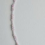 A delicate beaded necklace made of small, round pale pink and white beads, laid out in a curved line on a plain white background.