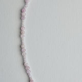 A delicate beaded necklace made of small, round pale pink and white beads, laid out in a curved line on a plain white background.