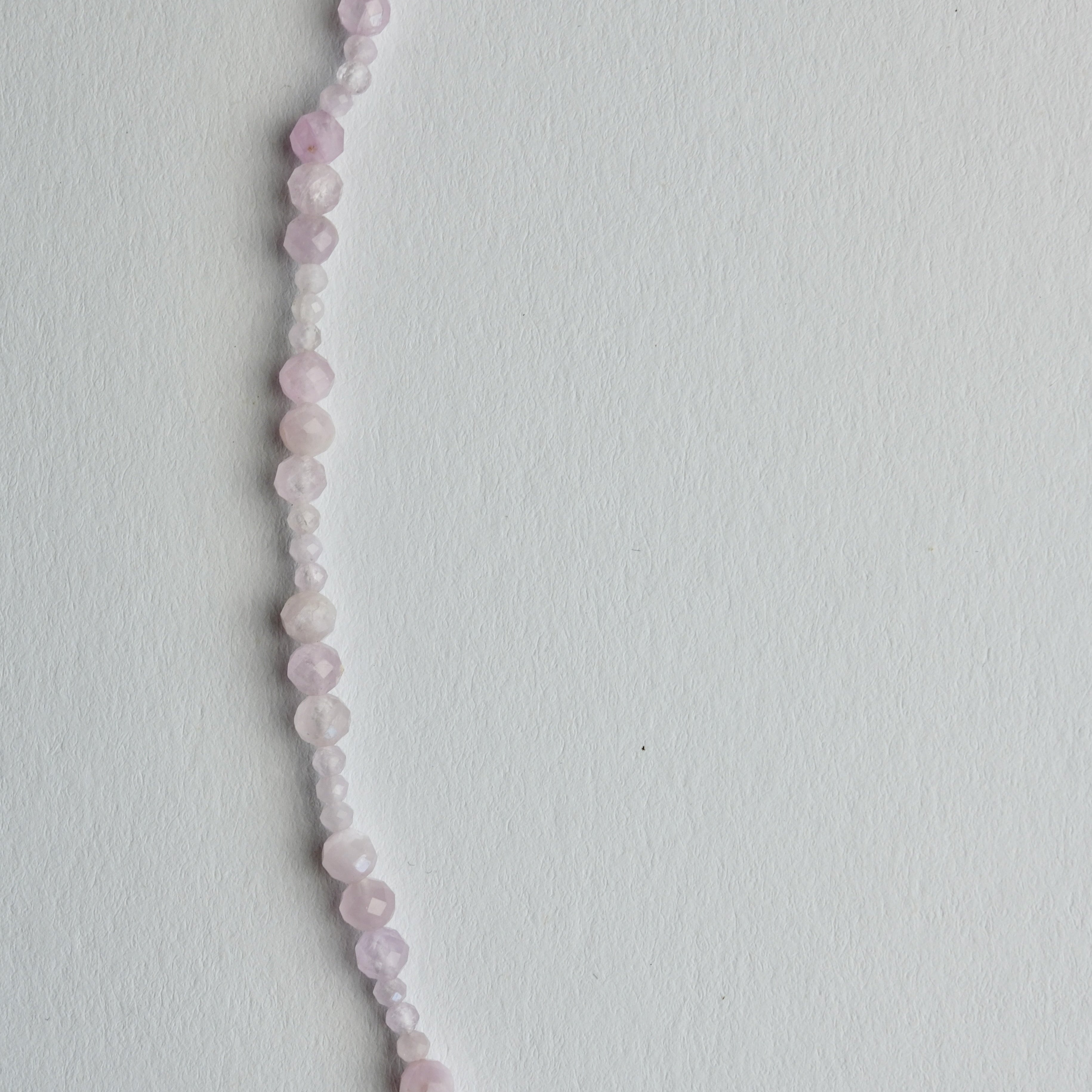 A delicate beaded necklace made of small, round pale pink and white beads, laid out in a curved line on a plain white background.