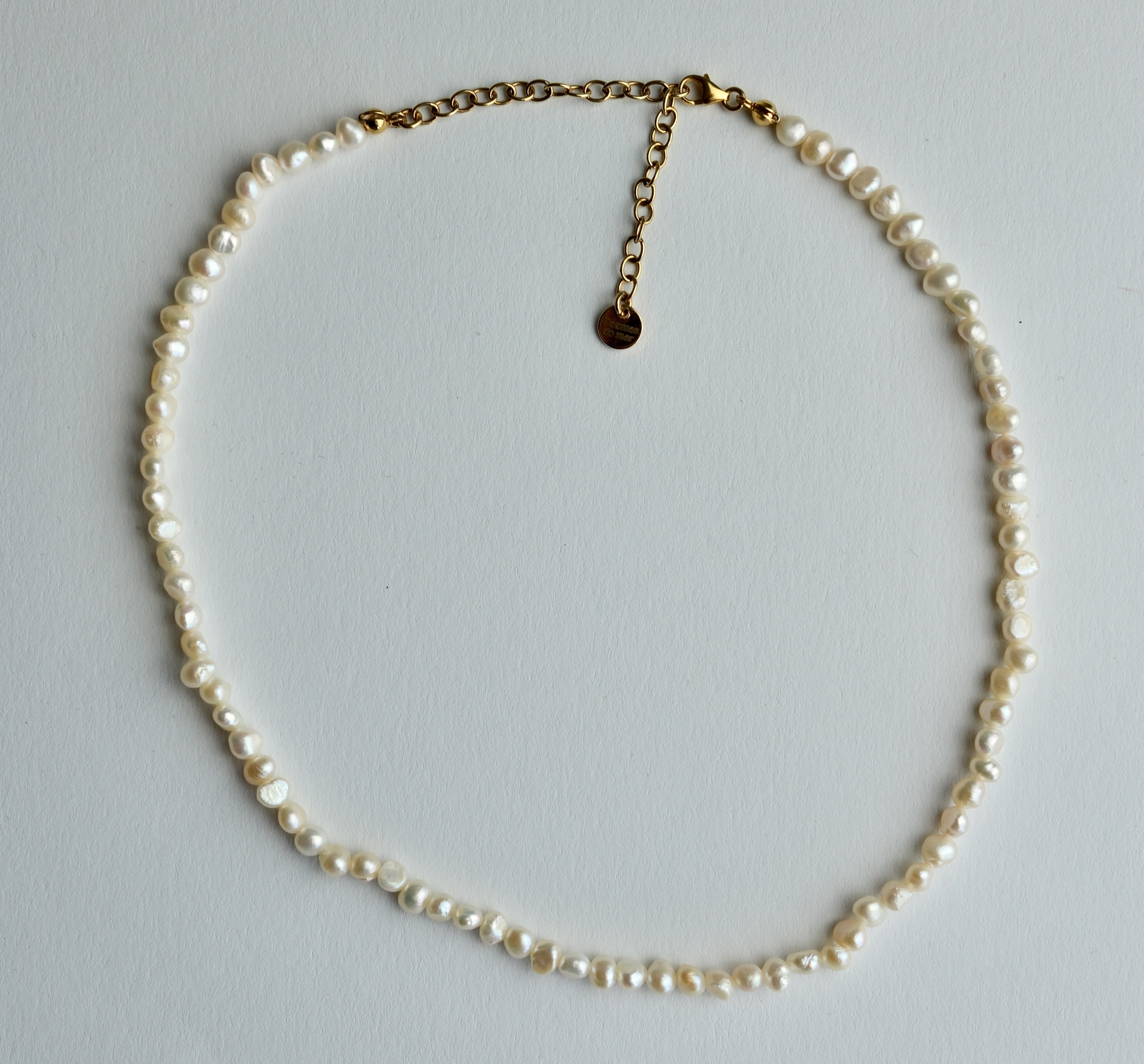 A single-strand pearl necklace with a gold chain extender and lobster clasp, laid flat on a light gray background.