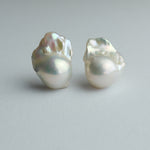 A pair of baroque pearl stud earrings on a neutral light gray background.