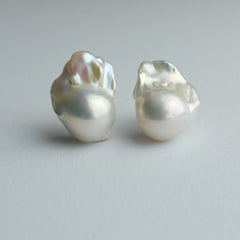 A pair of baroque pearl stud earrings on a neutral light gray background.