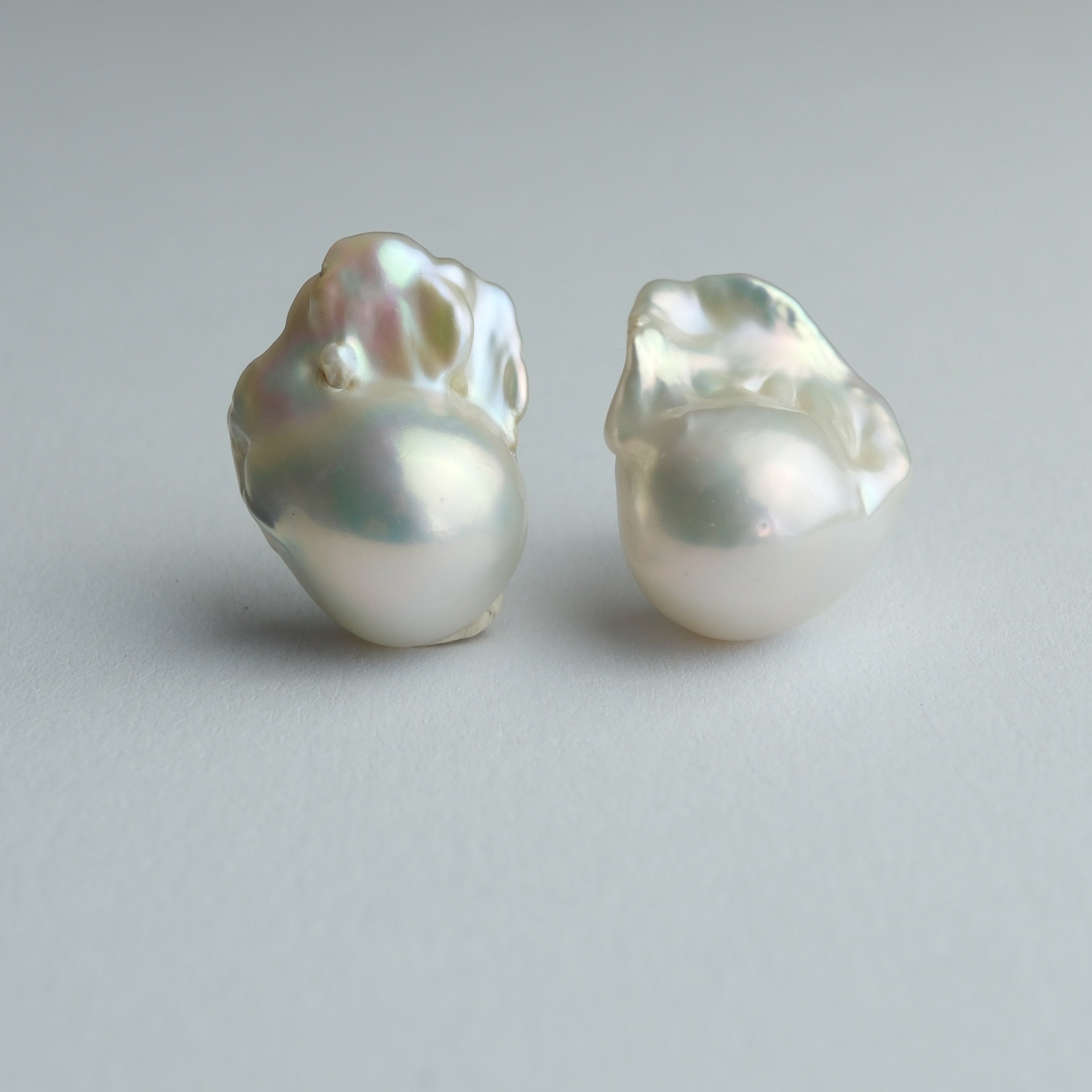 A pair of baroque pearl stud earrings on a neutral light gray background.