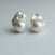 A pair of baroque pearl stud earrings on a neutral light gray background.