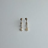 A pair of small gold huggie hoop earrings with dangling white freshwater pearls, shown on a plain light gray background.