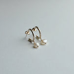A pair of gold huggie hoop earrings with dangling baroque pearl drops, photographed on a clean, light gray textured surface.