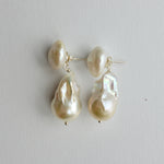 A pair of baroque pearl drop earrings with silver post settings, displayed on a neutral light gray background.