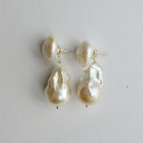 A pair of baroque pearl drop earrings with silver post settings, displayed on a neutral light gray background.