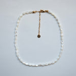 A white baroque pearl necklace with a gold chain extender and clasp, displayed on a light gray background.