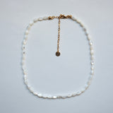 A white baroque pearl necklace with a gold chain extender and clasp, displayed on a light gray background.