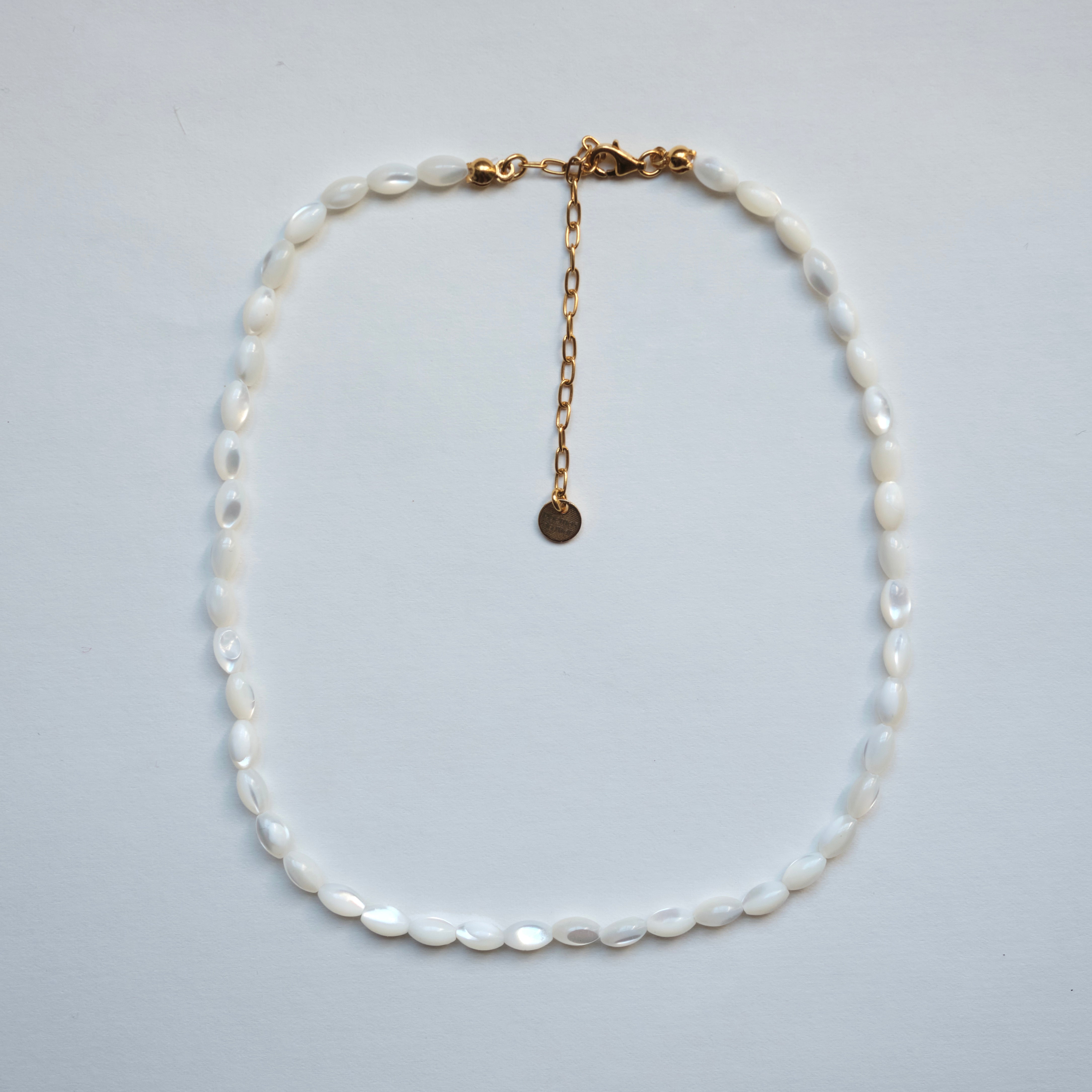 A white baroque pearl necklace with a gold chain extender and clasp, displayed on a light gray background.
