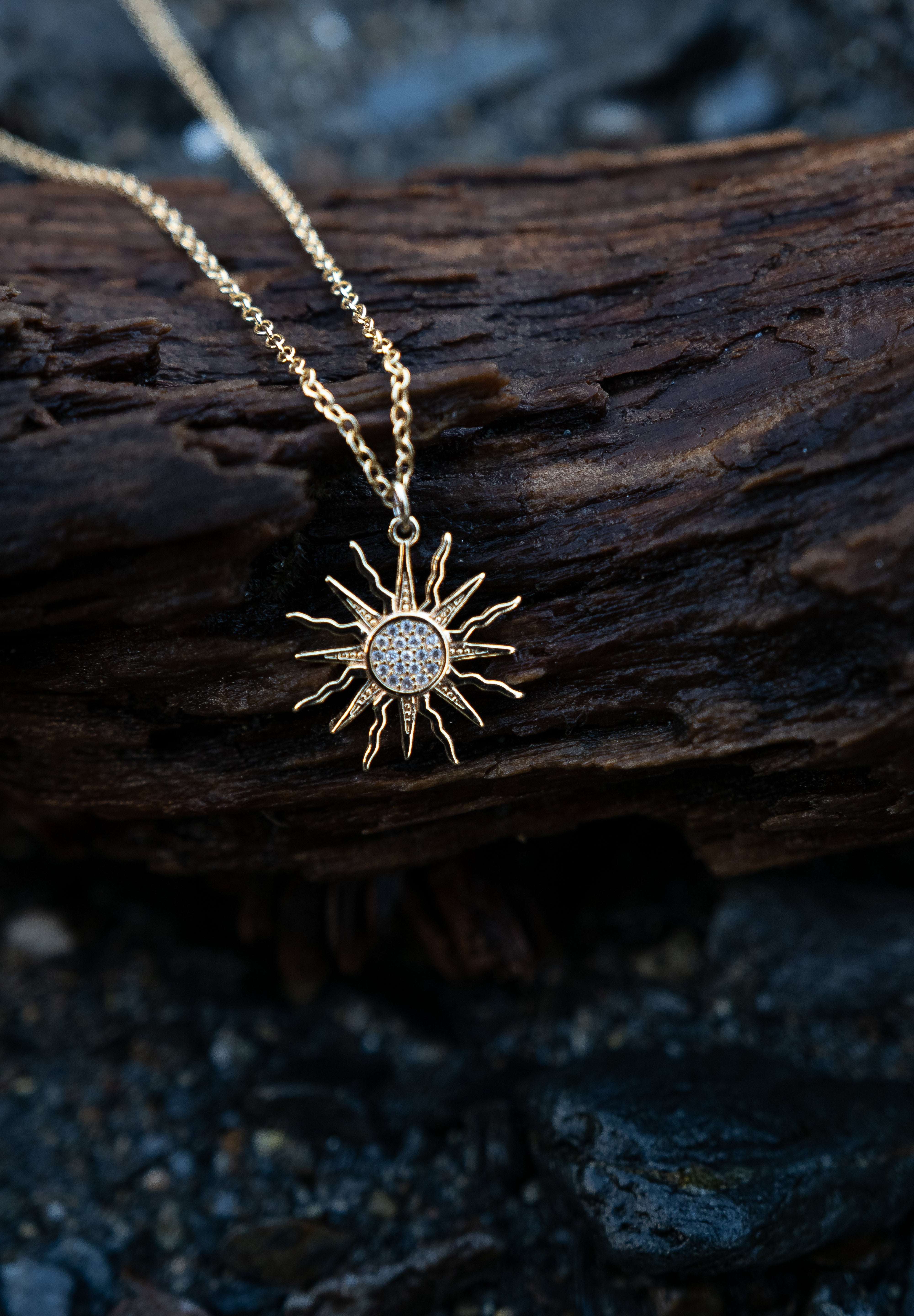 Gold sun-shaped pendant necklace on a wooden surface